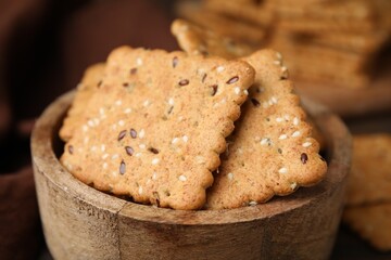 Cereal crackers with flax and sesame seeds in bowl on blurred background, closeup