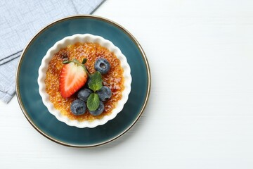 Delicious creme brulee with berries and mint in bowl on white wooden table, top view. Space for text