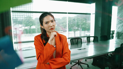 Professional young beautiful businesswoman thinking while standing at glass board with colorful sticky notes with marketing idea written. Portrait of project manager looking at mind map. Manipulator.