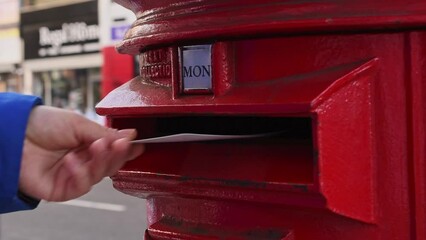 Sending a postcard. Close-up of a man's hand sending a postcard into a red postbox in London