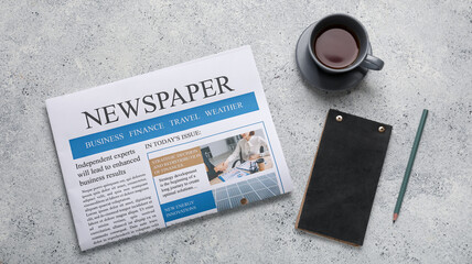 Newspaper with cup of tea, notebook and pencil on grunge background