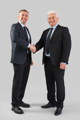 Mature brothers in suits shaking hands on grey background