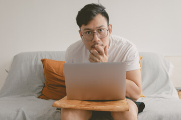 Asian man woking boring job with computer in his room sitting on the sofa. 
