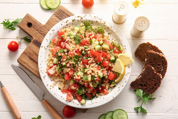 Plate with delicious tabbouleh salad and bread pieces on light wooden background