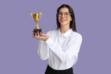 Young businesswoman with gold cup on lilac background