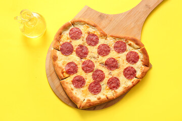Wooden board with tasty heart shaped pizza and oil on yellow background