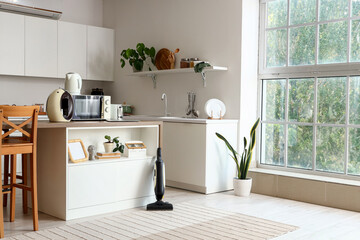 Wooden table with modern appliances, laptop and vacuum cleaner in contemporary kitchen