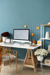 Interior of stylish home office with comfortable workplace, chrysanthemum flowers and pumpkins