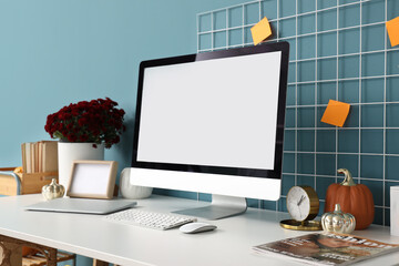 Comfortable workplace with modern computer, chrysanthemum flowers and pumpkins at home