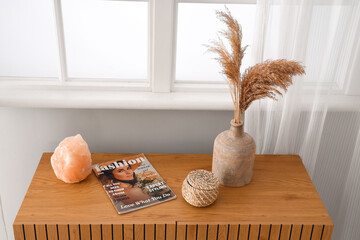 Vase with pampas grass, magazine and salt lamp on commode in living room