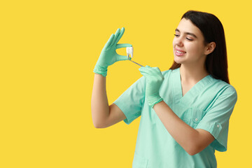 Female dentist with tool and plastic tooth on yellow background. World Dentist Day