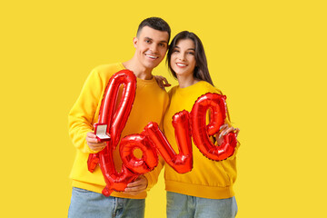 Young engaged couple with wedding ring and word LOVE made from balloons on yellow background....