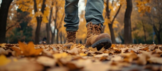 Man wearing winter boots strolling on fallen fall leaves.