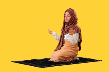 Little Muslim girl in hijab praying on yellow background