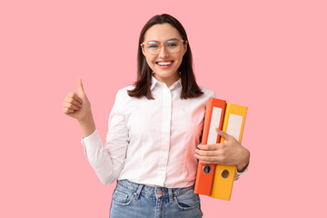 Young businesswoman with document folders showing thumb-up on pink background