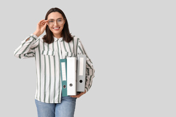 Young businesswoman with document folders on light background