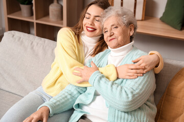 Young woman hugging her grandmother on sofa at home