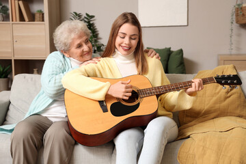 Senior woman hugging her granddaughter playing guitar at home