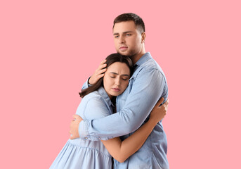 Sad young woman hugging her husband on pink background