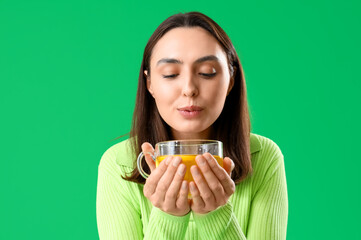 Young woman with cup of hot lemon tea on green background, closeup