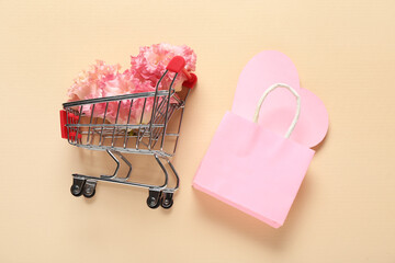 Small shopping cart with paper bag, heart and flowers on beige background. Valentine's Day celebration