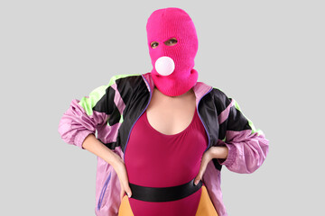 Beautiful young stylish woman in balaclava with gum on grey background