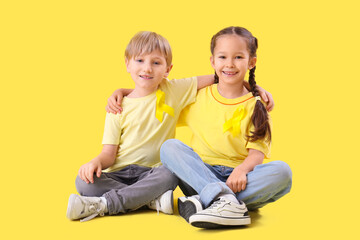 Cute little children with yellow ribbons on color background. Childhood cancer awareness concept