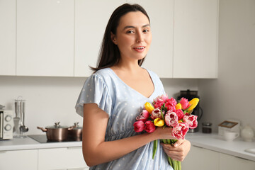 Young woman with bouquet of beautiful tulips in kitchen. International Women's Day