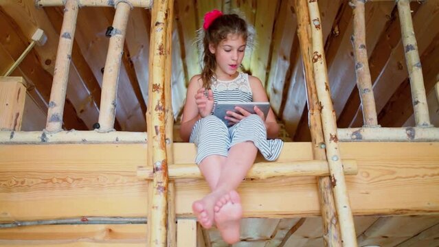 Young girl uses gadget during sits on stairs to second level of house