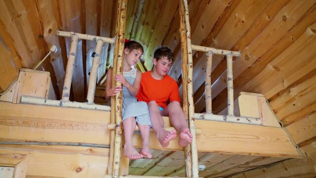 Barefoot kids boy and girl sit on second level of wooden house