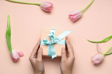 Female hands with gift box and beautiful tulips on pink background. International Women's Day
