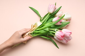 Female hand with bouquet of beautiful tulips on pink background. International Women's Day