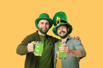 Happy young men in leprechaun hats with green beards holding glasses of beer on yellow background....