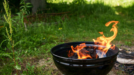 Black round Barbecue Grill with Fire on Open Air with green grass. Fire Flame. Prepairing charcoal...