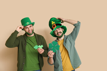 Happy young men in leprechaun hats with green beards holding clover on beige background. St....