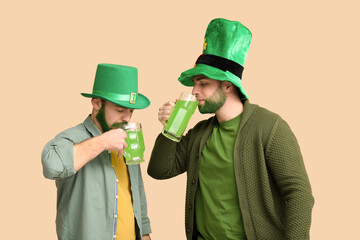 Young men in leprechaun hats with green beards drinking beer on beige background. St. Patrick's Day celebration