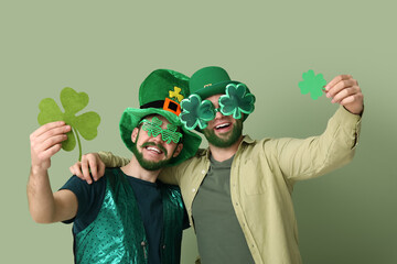 Young men in leprechaun hats and decorative glasses with green beards holding clover on green...