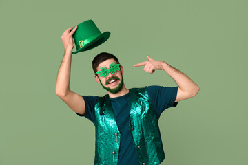 Young man with green beard pointing at decorative glasses in shape of clover and holding leprechaun...
