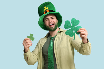 Young man in leprechaun hat with green beard holding clover on blue background. St. Patrick's Day...