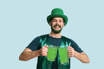 Young man in leprechaun hat with green beard holding glasses of beer on blue background. St. Patrick's Day celebration