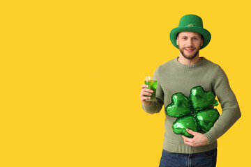 Happy young man in leprechaun hat with air balloon in shape of clover and glass of beer on yellow...
