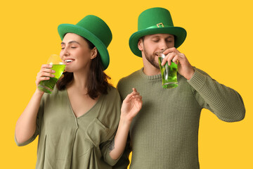 Beautiful young couple in leprechaun hats with glasses of beer on yellow background. St. Patrick's Day celebration