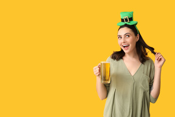 Happy young woman in leprechaun hat with glass of beer on yellow background. St. Patrick's Day...