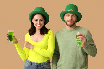 Beautiful young couple in leprechaun hats pointing at glasses of beer on brown background. St....