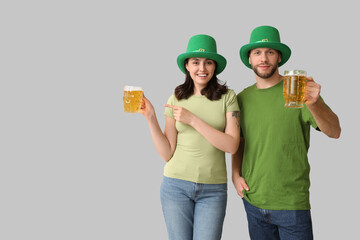 Beautiful young couple in leprechaun hats pointing at glasses of beer on grey background. St....