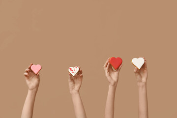 Women with heart-shaped cookies on brown background. Valentine's Day celebration