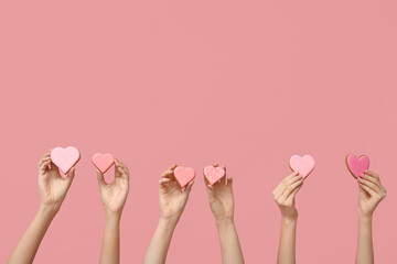 Women with heart-shaped cookies on pink background. Valentine's Day celebration