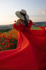 Woman poppy field red dress hat. Happy woman in a long red dress in a beautiful large poppy field....