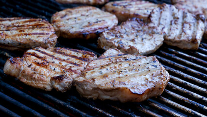 Grilled meat steak on stainless BBQ grill with flames on dark background. Food and cuisine concept.