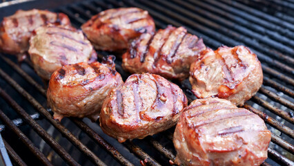 Grilled meat steak wrapped in bacon on stainless BBQ grill with flames on dark background. Food and cuisine concept.
